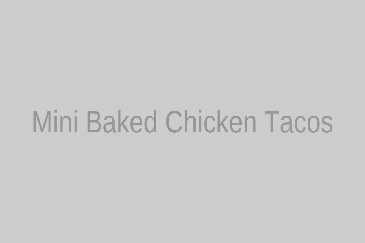 Mini baked chicken tacos arranged on a baking sheet with melted cheese and fresh toppings