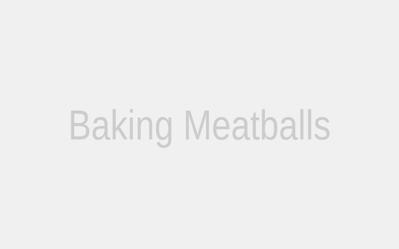 A baking sheet filled with Asian Meatballs halfway through their baking time in the oven, showing slight browning and even cooking.